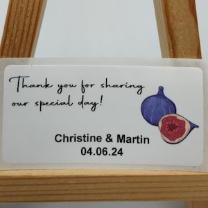 Op de afbeelding: Witte bedankkaart met een afbeelding van een blauwe en rode vijg. De kaart zegt "Bedankt voor het delen van onze speciale dag!" en "Christine & Martin 04.06.24".