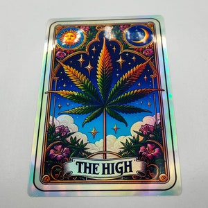 May include: A holographic sticker featuring a colourful illustration of a cannabis leaf surrounded by stars, clouds and flowers. The text "THE HIGH" is written on a banner below the leaf.