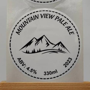 May include: Two white round stickers with black text and a mountain range graphic. The text reads "Mountain View Pale Ale", "ABV: 4.5%", "330ml", and "2023".