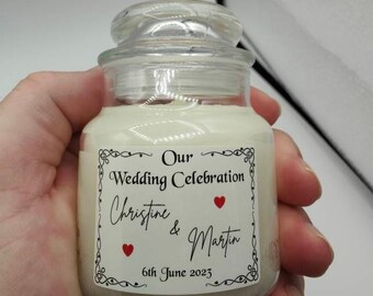 May include: A clear glass jar candle with a white label that reads "Our Wedding Celebration Christine & Martin 6th June 2023". The label has a decorative border and two red hearts.