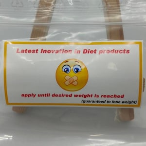 May include: A yellow and white label with a cartoon smiley face with a bandage over its mouth. The label reads "Latest Innovation in Diet products apply until desired weight is reached (guaranteed to lose weight)"