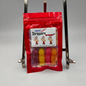 K&ouml;nnte beinhalten: Ein wiederverschlie&szlig;barer Beutel aus rotem Material mit einem Sichtfenster, in dem drei bunte Gummib&auml;rchen in Menschenform zu sehen sind. Der Beutel hat ein wei&szlig;es Etikett mit dem Text "Some Xmas Strippers Ho-ho-ho! Lick, Suck or nibble without getting into trouble!"
