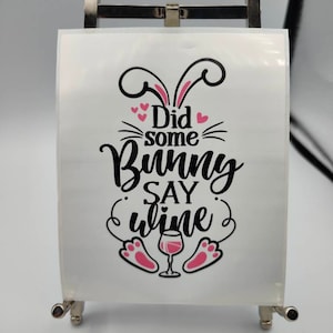 Peut inclure: Un autocollant en vinyle blanc avec un motif noir et rose. Le motif représente un lapin avec le texte "Did some bunny say wine?" et un verre de vin.