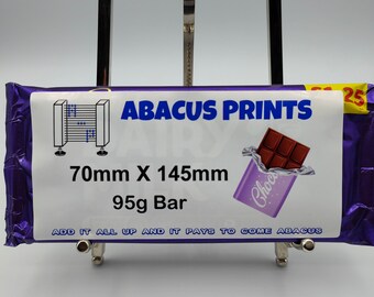 Può includere: Un involucro di cioccolato viola e bianco con il testo "ABACUS PRINTS" e "70mm X 145mm 95g Bar". L'involucro include anche una piccola immagine di una barretta di cioccolato e il testo "ADD IT ALL UP AND IT PAYS TO COME ABACUS".