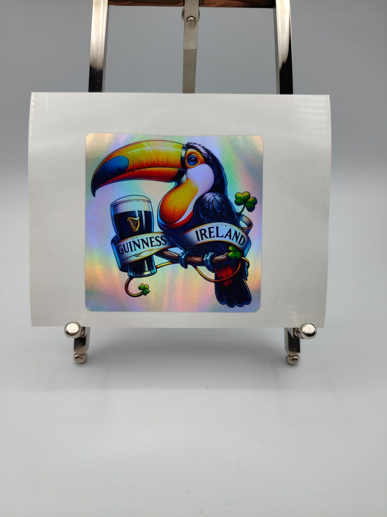 Op de afbeelding: Een kleurrijke toekan die een glas Guinness-bier vasthoudt met de tekst "IRELAND" en "GUINNESS" op een holografische sticker.