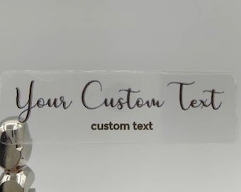 May include: Clear, rectangular sticker with the text "Your Custom Text" in black cursive font. The text "custom text" is also printed in black below the cursive text.