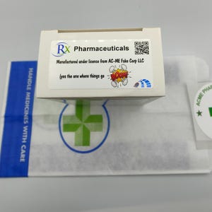 Może przedstawiać: Białe pudełko z niebiesko-zielonym logo z napisem "RX Pharmaceuticals". Pudełko zawiera kod QR i tekst "Manufactured under licence from AC-ME Fake Corp LLC (yes the one where things go BOOM!)"