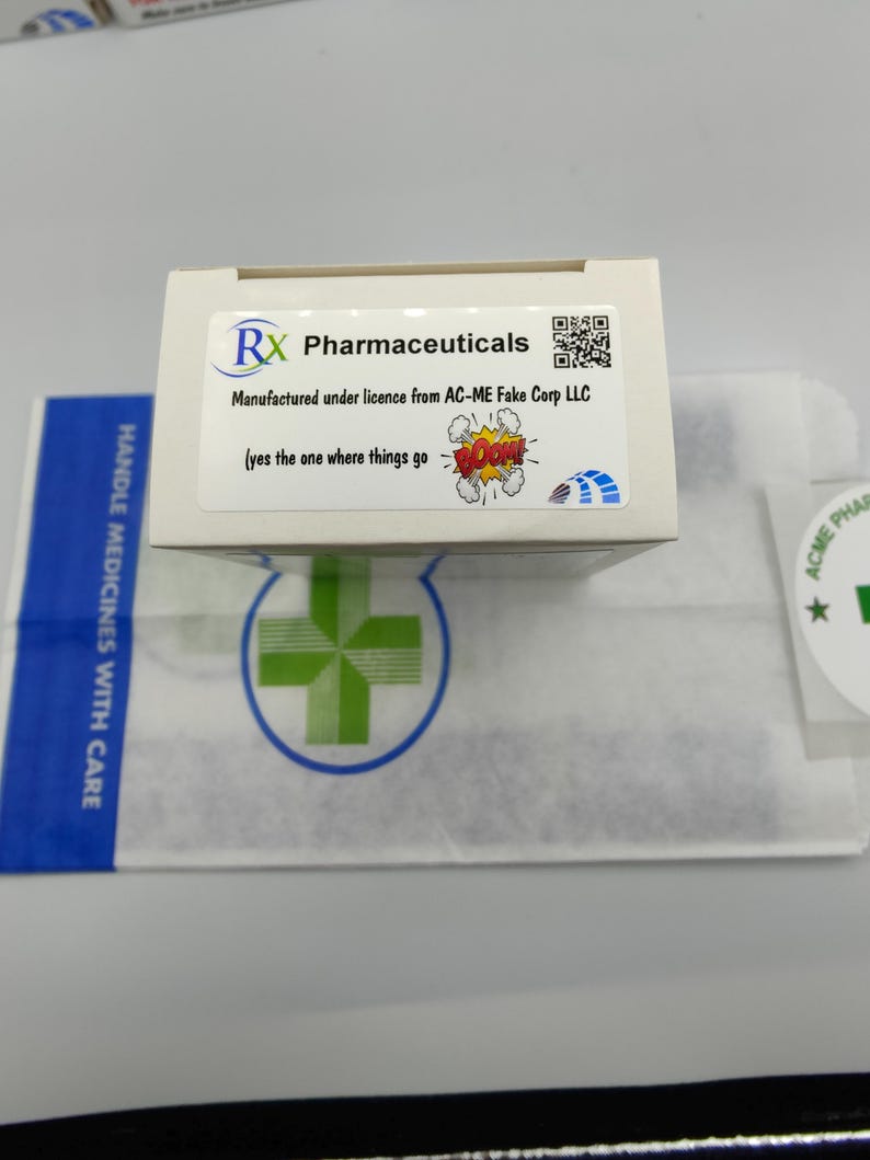 Może przedstawiać: Białe pudełko z niebiesko-zielonym logo z napisem "RX Pharmaceuticals". Pudełko zawiera kod QR i tekst "Manufactured under licence from AC-ME Fake Corp LLC (yes the one where things go BOOM!)"