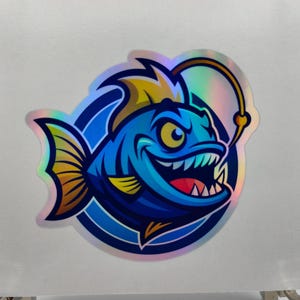 Può includere: Un adesivo olografico raffigurante un pesce lanterna dei cartoni animati con un'espressione minacciosa. Il pesce è principalmente blu con accenti gialli e dorati, su uno sfondo circolare. Il pesce lanterna ha denti affilati e un'esca luminosa.