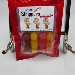 K&ouml;nnte beinhalten: Ein wiederverschlie&szlig;barer roter Beutel mit einem Sichtfenster, in dem bunte Gummib&auml;rchen in Form von Weihnachtsm&auml;nnern zu sehen sind. Der Beutel hat ein Etikett mit der Aufschrift "Some Xmas Strippers" mit einem Bild von drei Weihnachtsm&auml;nnern und dem Text "Ho Ho Ho!"  Das Etikett sagt auch "Lick, Suck or Nibble without getting into trouble!"