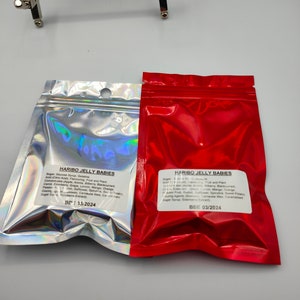 K&ouml;nnte beinhalten: Zwei rote und silberne Folienbeutel mit Haribo Jelly Babies S&uuml;&szlig;waren. Der rote Beutel hat ein Mindesthaltbarkeitsdatum vom 03/2024. Der silberne Beutel hat ein Mindesthaltbarkeitsdatum vom 13/2024. Die Beutel sind mit den Zutaten und N&auml;hrwertangaben gekennzeichnet.