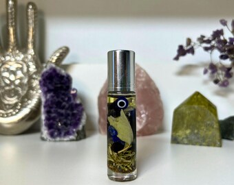 May include: A clear glass roller bottle with a silver cap filled with a yellow liquid and various blue and white charms, including an evil eye charm.