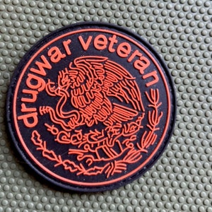 May include: Black and orange embroidered patch with the text "drug war veteran" and a stylized image of an eagle.