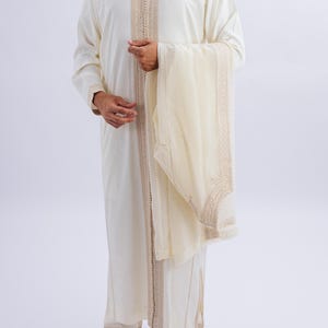 May include: A white long-sleeved robe with gold embroidery and a matching white scarf. The robe has a high collar and a long, flowing design.