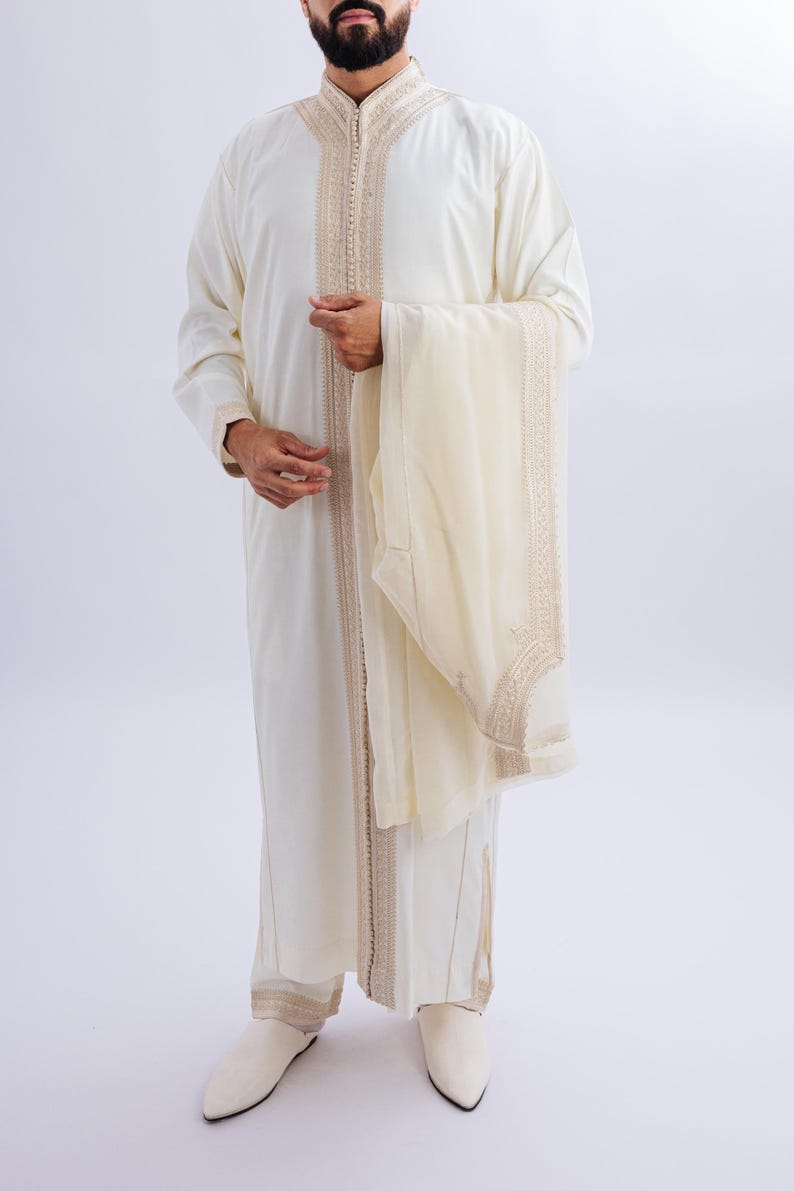 May include: A white long-sleeved robe with gold embroidery and a matching white scarf. The robe has a high collar and a long, flowing design.
