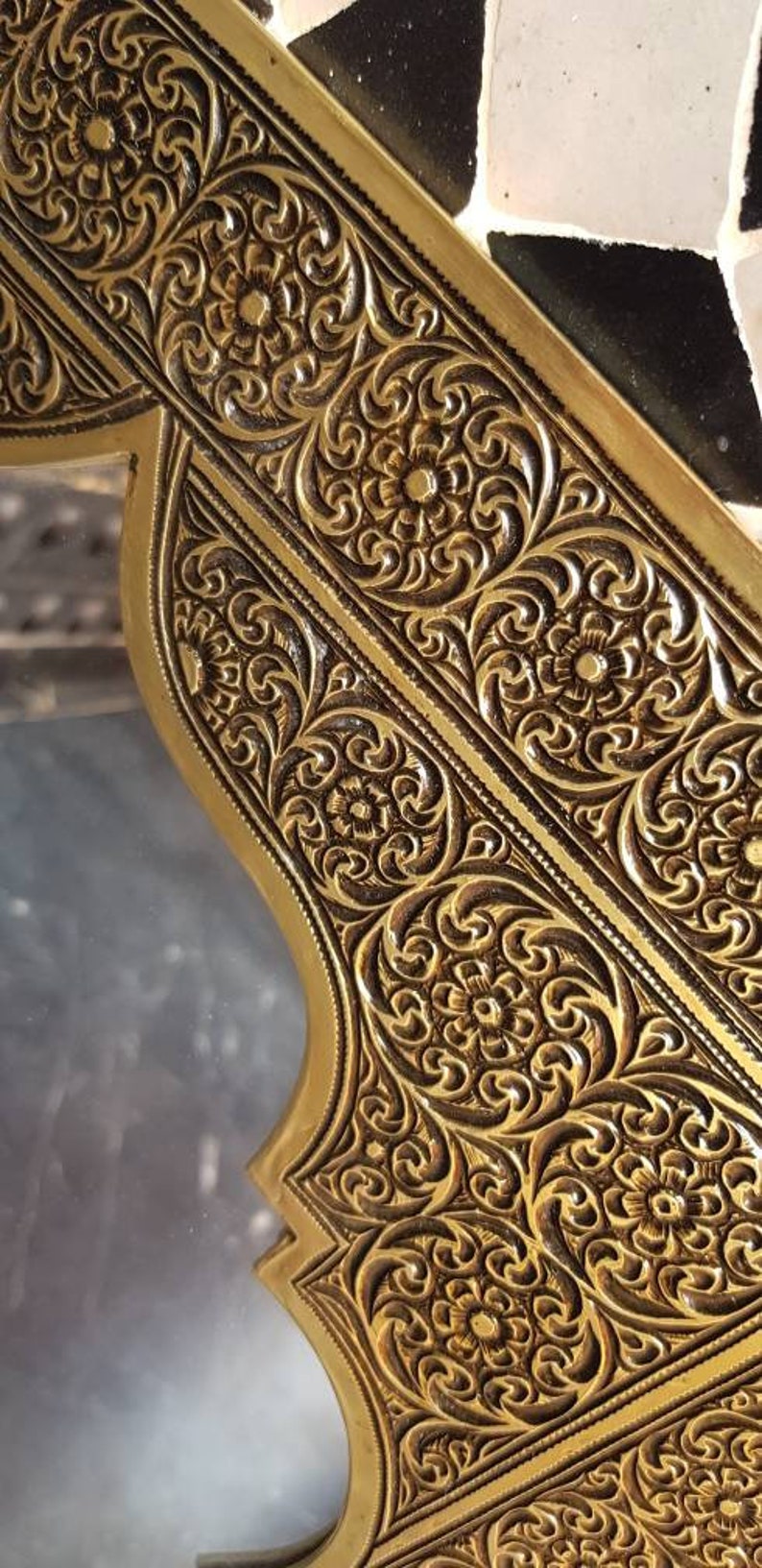 Pode incluir: Close-up de uma moldura de metal dourada com intrincados desenhos florais. A moldura tem uma superf&iacute;cie texturizada em relevo e uma forma ligeiramente curva.