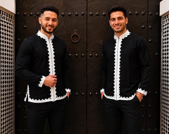 May include: Two men wearing black shirts with white trim and detailing. The shirts have a mandarin collar and are paired with black pants. The outfits are traditional in style and are suitable for formal occasions.