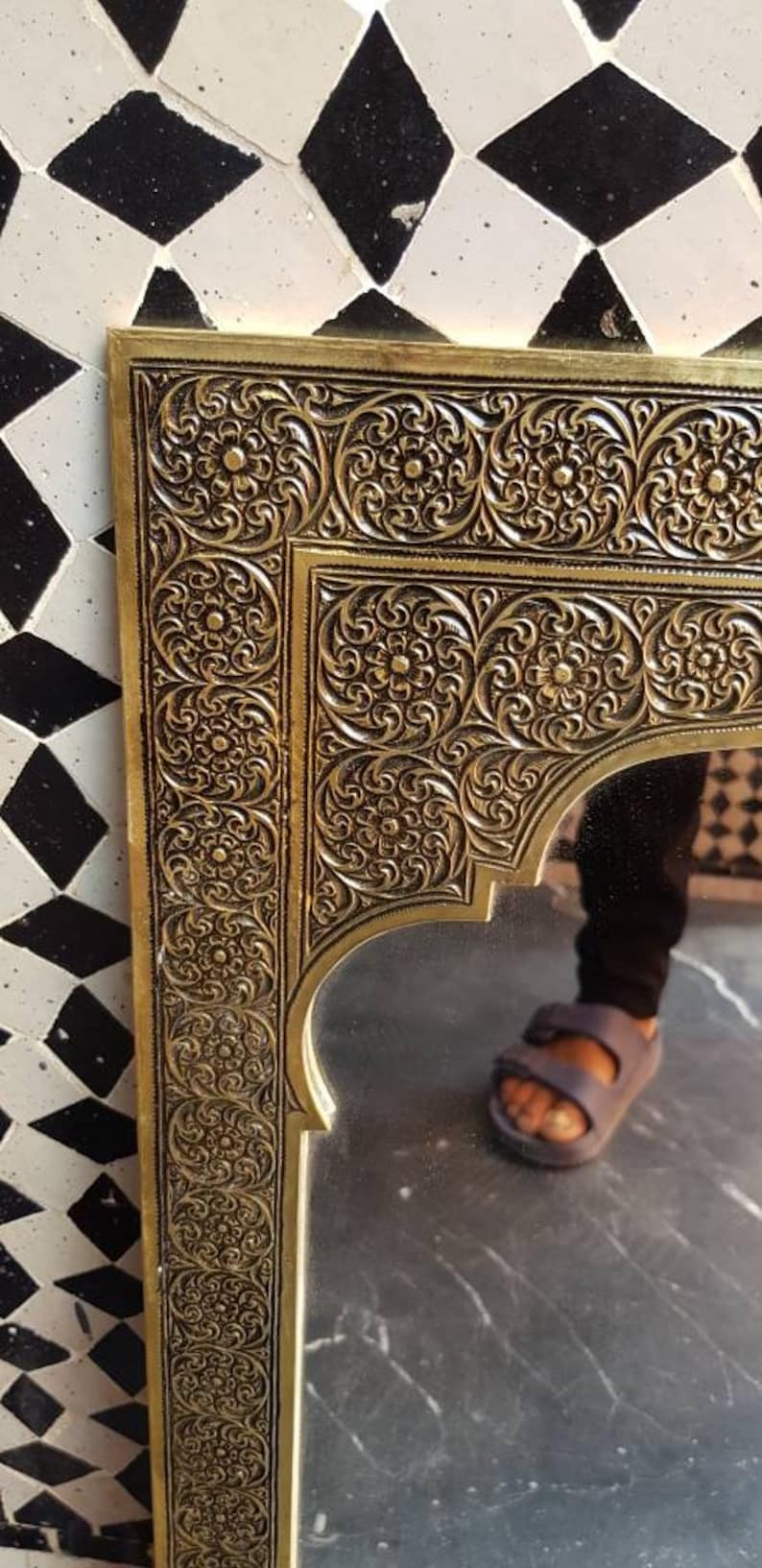 Pode incluir: Um espelho de metal dourado com um design ornamentado, intrincado e detalhado. O espelho tem uma forma de arco marroquino tradicional e &eacute; emoldurado por uma moldura decorativa.