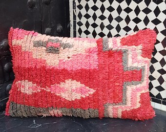 May include: A red, pink, and gray patterned throw pillow with a woven texture. The pillow is made of a soft, plush material and has a rectangular shape.