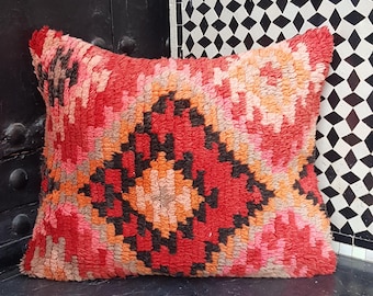 May include: A red, pink, orange, and black patterned throw pillow with a geometric design. The pillow is made of a soft, fuzzy material.