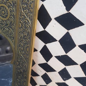K&ouml;nnte beinhalten: Ein verzierter Spiegelrahmen in Gold mit aufwendigen floralen Mustern. Der Rahmen ist vor einem Hintergrund aus schwarzen und wei&szlig;en Diamantenfliesen platziert.