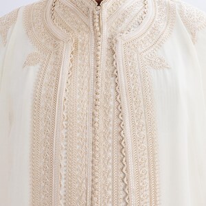 May include: A white robe with intricate gold embroidery around the collar and down the front. The robe has a button closure.