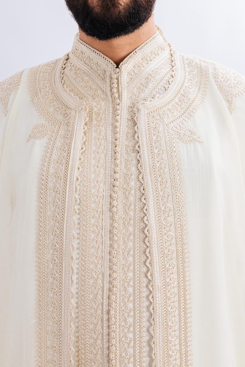 May include: A white robe with intricate gold embroidery around the collar and down the front. The robe has a button closure.