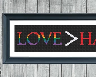 Könnte beinhalten: Ein gerahmtes Kreuzstich-Design mit den Worten "LOVE>HATE" in Regenbogen- und roter Schrift auf schwarzem Hintergrund.