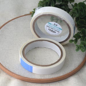 May include: Two rolls of 3/4 inch double-sided acid-free finishing tape. The tape is white and has a blue label with the text "3/4" Finishing Tape Double-Sided Acid-Free".