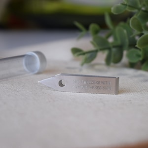 May include: Silver tweezers with a pointed tip and the text "THE TWEEZERS WITH PIN-POINT-PRECISION" engraved on the side.