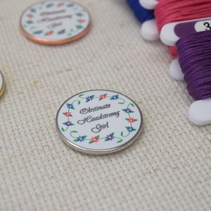 Puede incluir: Un disco redondo blanco con un borde floral y el texto "Obstinate Headstrong Girl" en letras negras. El disco es de metal y tiene un acabado plateado.