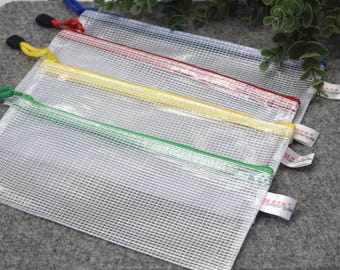 Könnte beinhalten: Vier transparente Netztaschen mit farbigen Reißverschlüssen in Grün, Gelb, Rot und Blau. Jede Tasche hat einen farblich passenden Reißverschlussanhänger und ein kleines weißes Etikett. Die Taschen sind diagonal auf einer grauen Oberfläche angeordnet.