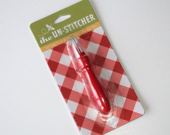Könnte beinhalten: Ein rotes und silbernes Nähfaden-Entfernungstool, verpackt auf einem weißen und roten Gingham-Hintergrund. Die Verpackung trägt den Text "i{heart} UN-STITCHER by Lori Holt of Bee in My Bonnet Co."