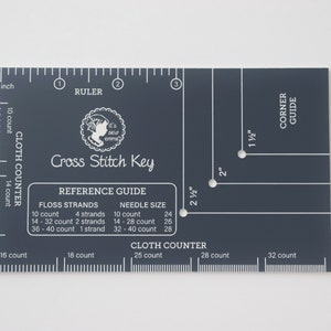 May include: A black plastic cross stitch key with a ruler, cloth counter, and corner guide. It includes a reference guide for floss strands and needle sizes. The text on the key reads "Cross Stitch Key", "Reference Guide", "Floss Strands", "Needle Size", "Cloth Counter", and "Corner Guide".