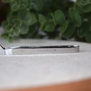 May include: A silver metal tool with a pointed tip and the words "CLOVER STAINLESS" engraved on the side. The tool is lying on a light brown surface.