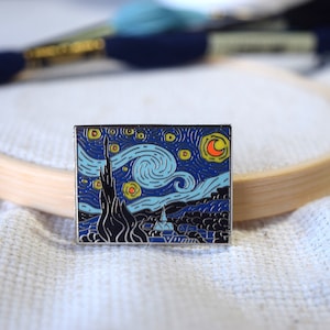 May include: A silver enamel pin featuring a recreation of Vincent van Gogh's famous painting, "The Starry Night". The pin depicts a swirling night sky with a crescent moon and stars in shades of yellow, blue, and orange.