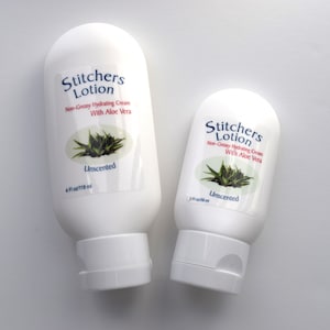 May include: Two white plastic bottles of unscented lotion labeled "Stitchers Lotion" with a green aloe vera plant graphic. The larger bottle is 4 fl oz/118 ml and the smaller bottle is 2 fl oz/59 ml.