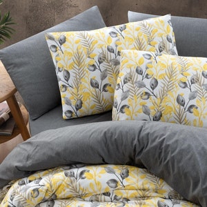 May include: A white duvet cover with a yellow and gray leaf pattern. The duvet cover is on a bed with two gray pillowcases and two yellow and gray patterned pillowcases. A wooden bowl with fruit is on the bed.