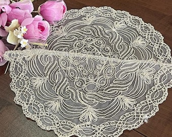 May include: A white crocheted doily with a delicate floral design. The doily is round and has a scalloped edge.