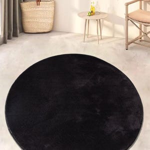 Puede incluir: Una alfombra redonda y esponjosa de color negro con una textura suave. La alfombra está sobre un suelo gris claro.