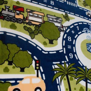 May include: A white play mat with a blue road and green grass. The road has white dashed lines and a train with three cars. There is a yellow car driving on the road. The mat has the math problems 4 + 4 = 8 and 1 + 8 = 9.