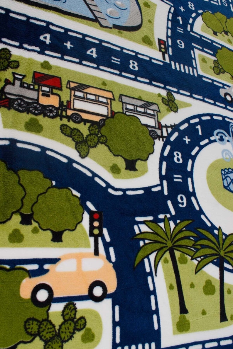 May include: A white play mat with a blue road and green grass. The road has white dashed lines and a train with three cars. There is a yellow car driving on the road. The mat has the math problems 4 + 4 = 8 and 1 + 8 = 9.