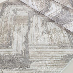May include: A white and gray area rug with a geometric pattern. The rug has a soft, plush texture and a subtle sheen.