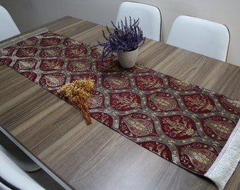 Könnte beinhalten: Ein Tischläufer in Burgunderrot und Silber mit einem traditionellen türkischen Muster. Der Läufer hat an beiden Enden einen weißen Fransen und liegt auf einem Holztisch.