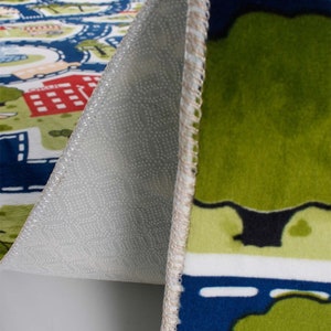 May include: Close-up of the underside of a colorful play rug with a city scene. The rug has a non-slip backing with small white dots.
