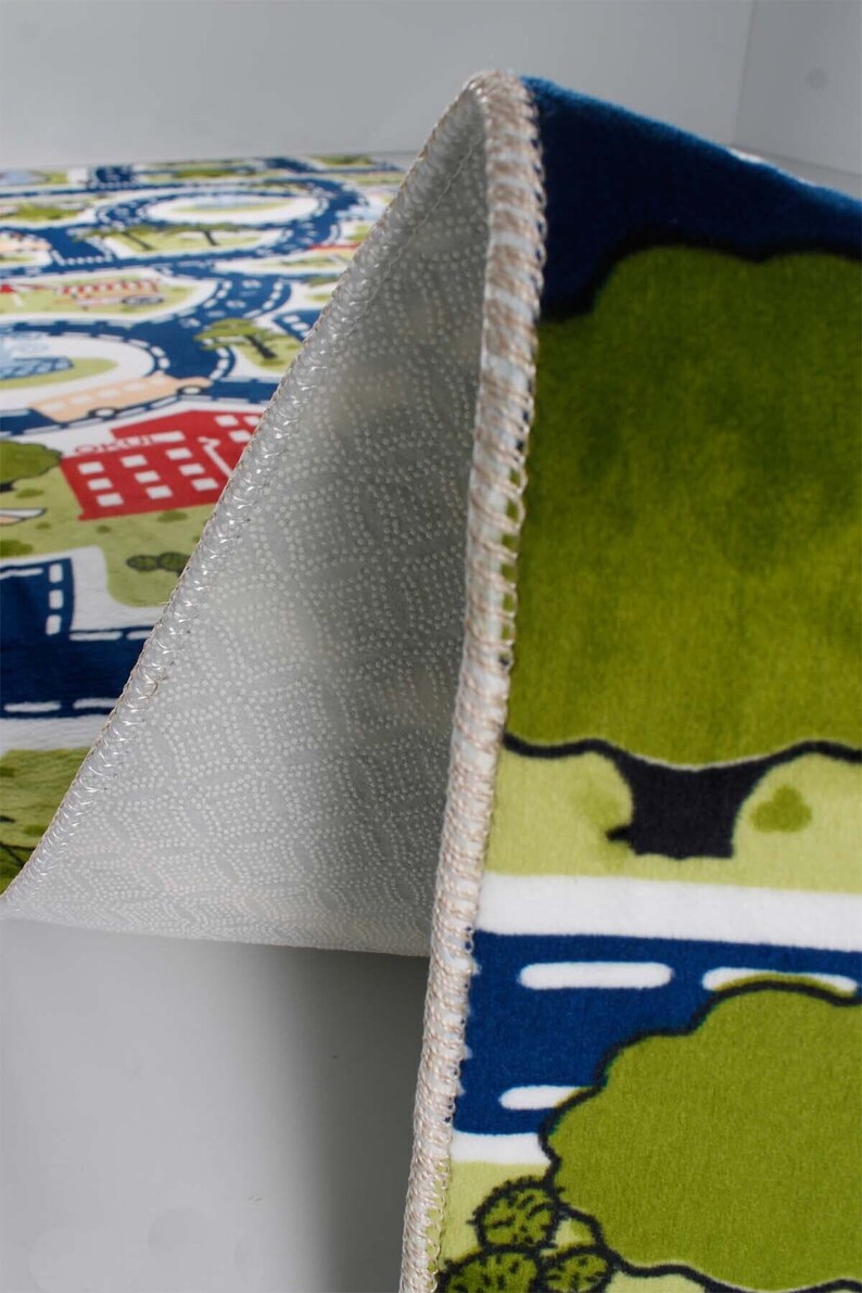 May include: Close-up of the underside of a colorful play rug with a city scene. The rug has a non-slip backing with small white dots.
