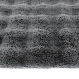 May include: Close-up of a plush, gray faux fur fabric. The fabric has a wavy texture, creating a soft, inviting appearance. The edges are neatly finished with a sewn border, suggesting a finished product like a blanket or rug.