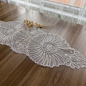 May include: White crocheted table runner with a delicate floral design. The runner features two large circular motifs with intricate patterns.