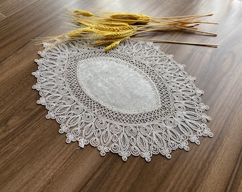 May include: White lace doily with a delicate floral pattern. The doily is circular with a center oval opening.