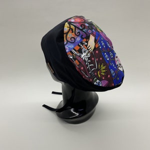 Könnte beinhalten: Schwarze OP-Mütze mit einem farbenfrohen Muster, das eine Frau, Blumen und geometrische Formen zeigt. Die Mütze hat verstellbare Bänder.